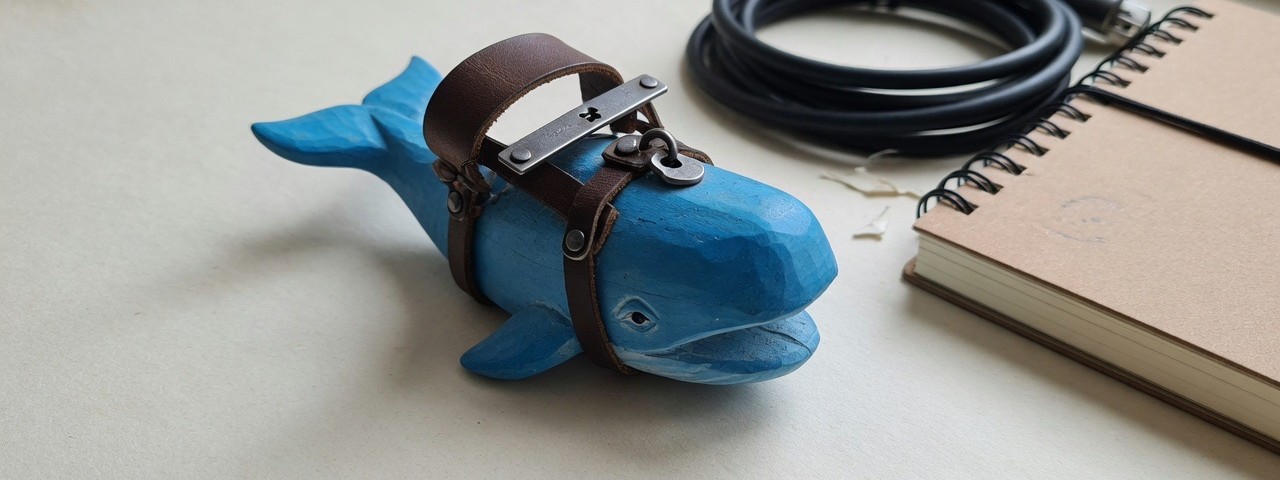 A carved blue whale in a leather harness beside cables and a laptop: DeepSeek's whale, Harness's yoke